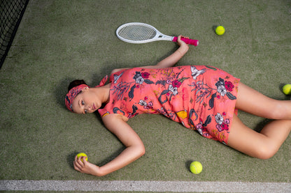 Woman in a floral dress lying on a tennis court with a racket and balls around her.